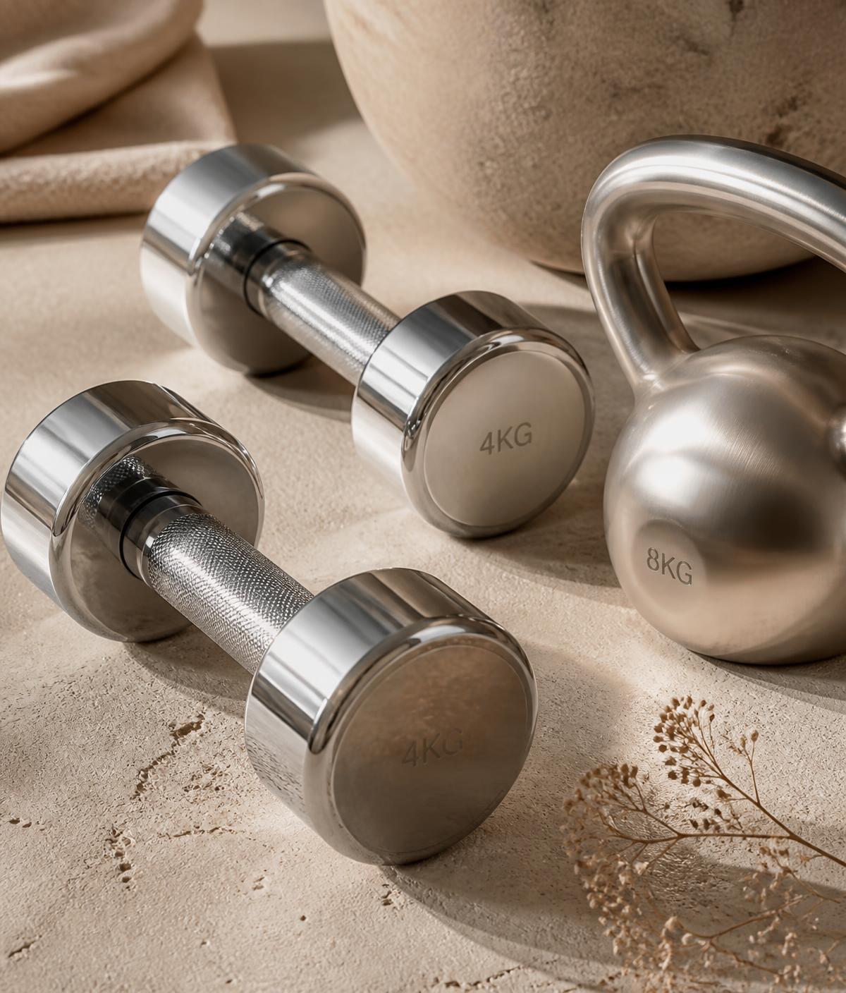 Chrome dumbbells and a kettlebell arranged on a warm stone surface